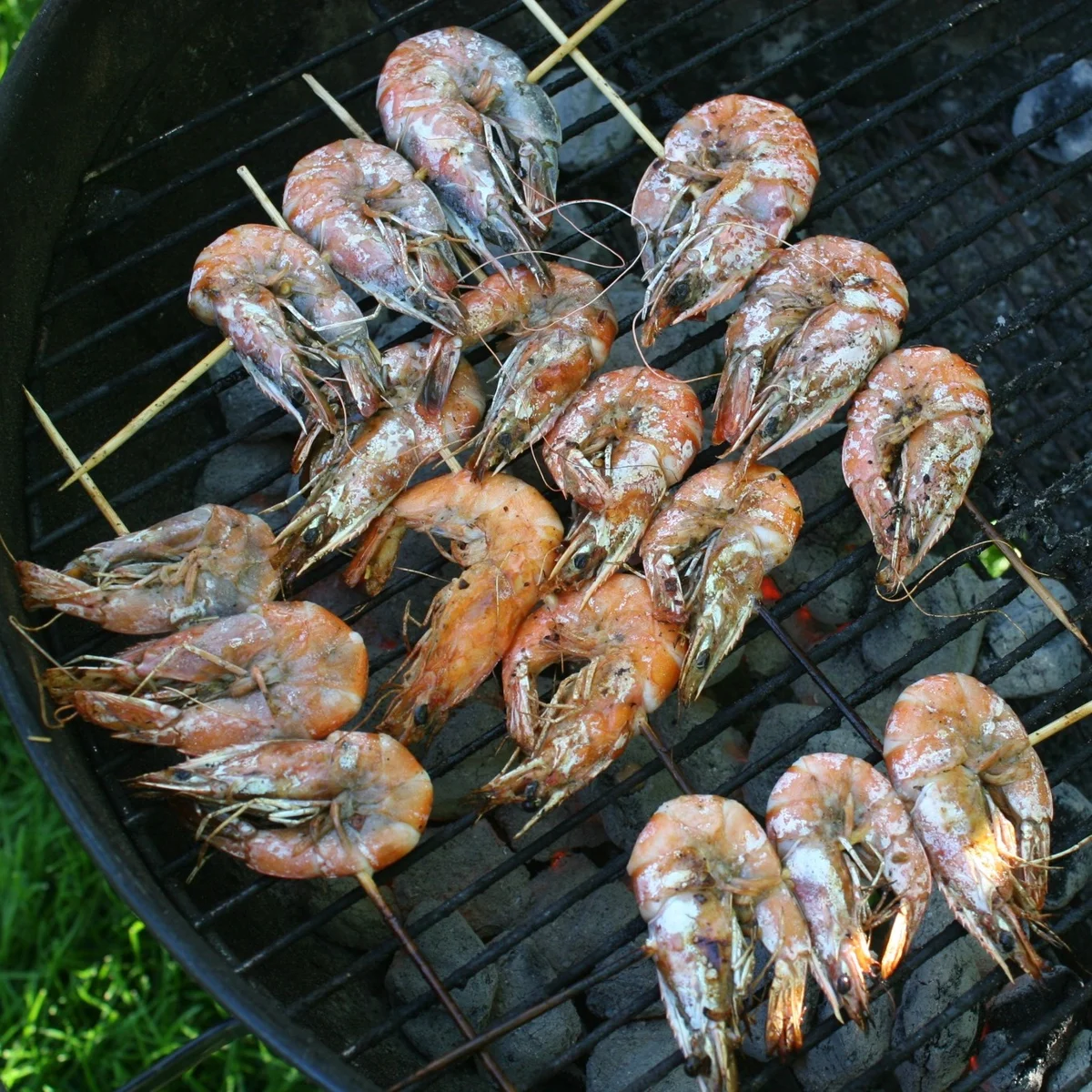 Whole shrimp on skewers cooking over a grill.